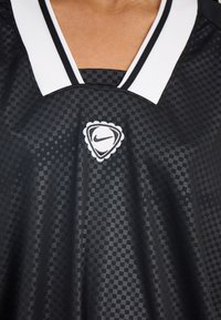 Black Nike jersey featuring a checkered pattern, white collar, and a logo in the center with a triangular outline and scalloped edge.