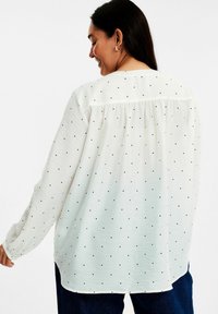 Vit långärmad blus med små svarta prickar, en avslappnad passform, veckad ryggdetalj och elastiska manschetter.