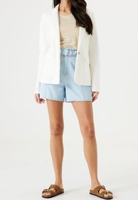 Biała marynarka na beżowo-białym, paskowanym topie, do tego jasnoniebieskie szorty. Brązowe sandały z ozdobnymi detalami.