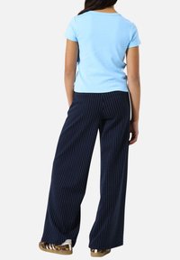 Chemise slim bleu clair à manches courtes associée à un pantalon large à rayures bleu marine, avec un tissu texturé subtil et des rayures blanches contrastées.