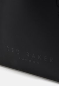 Gros plan d'une surface noire avec le logo "TED BAKER LONDON" imprimé dans une lettrage sombre et subtil.