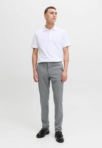 Camisa polo blanca con cuello, combinada con pantalones ajustados gris claro. Zapatos negros con detalles decorativos. Diseño simple y limpio.