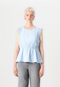 Hele helesinine peplum-top, millel on pitsäärised õlgadel, ümar kaelus ja kokkusurutud vöökoht. Kombineeritud hallide teksadega. Sile kangastekstuuri.