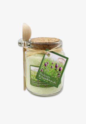 Glasgefäß, gefüllt mit hellgrünem Badesalz, Korkdeckel, Holzlöffel und grünem Etikett mit Lavendel und Produktdetails.