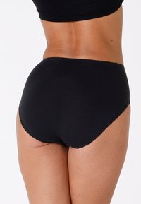 Mutande nere a vita alta realizzate in tessuto liscio e elastico. Presentano bordi ondulati e un design senza cuciture per comfort e vestibilità.