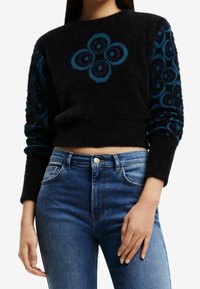 Svart croppad tröja med blått blommönster på fram- och ärmar; mjuk textur, rund halsringning, passform kombinerad med högmidjade blå jeans.