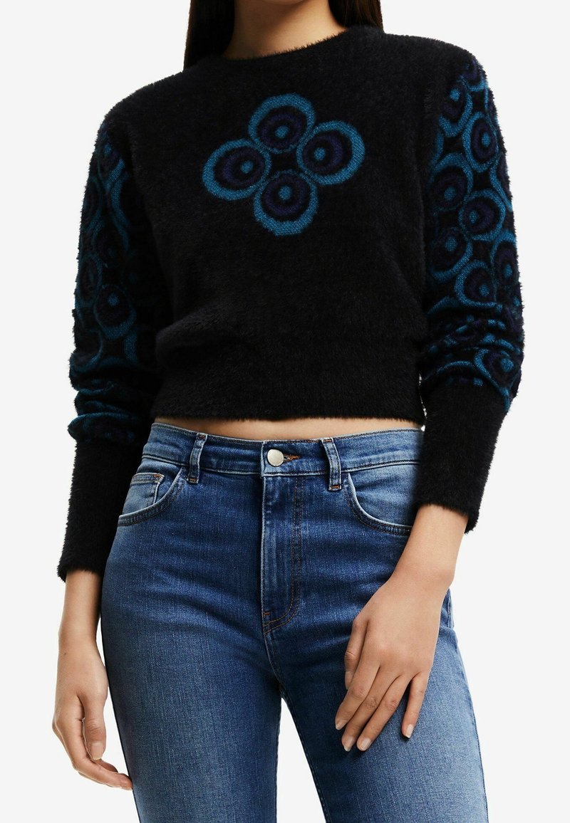 Svart croppad tröja med blått blommönster på fram- och ärmar; mjuk textur, rund halsringning, passform kombinerad med högmidjade blå jeans.