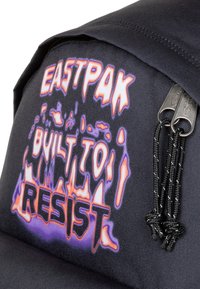 Mochila de tela negra con gráficos audaces y multicolores que dicen "EASTPAK BUILT TO RESIST", con dobles cremalleras y superficie texturizada.