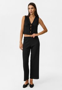 Zwart textuur tweedelig outfit met een cropped mouwloos top met een vetersluiting aan de voorkant en loszittende broek.