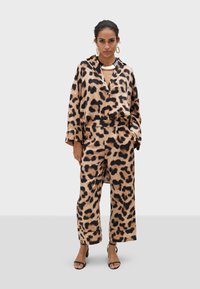 Ensemble imprimé léopard en tissu doux, comprenant une veste ample avec capuche et un pantalon large. Accents noirs et bijoux audacieux.