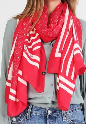 Écharpe rouge et blanche à motifs floraux et rayures portée sur une chemise gris clair boutonnée et un jean bleu.