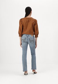 Blusa de algodón marrón con mangas abullonadas, combinada con jeans de color azul claro que tienen bolsillos traseros bordados y dobladillos deshilachados. Tacones negros de punta abierta.