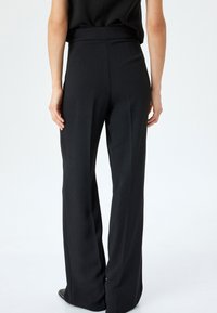 Zwarte brede broek met hoge taille, zachte textuur en zijzakken. Achteraan zijn de strakke lijnen en het op maat gemaakte ontwerp goed zichtbaar.