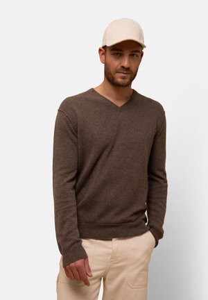 Brown v-neck sweater made of soft material, featuring long sleeves and a ribbed hem, paired with light-colored pants and a beige cap.