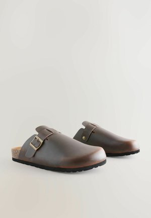 Ruske nahkaste klumpi ümarate varvastega, külgmise pandlaga ja korkalusega. Tekstuuriga kummitald haardeks. Minimalistlik disain.