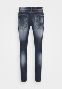 Jeans ajustados en denim índigo oscuro con un lavado desvaído, que cuentan con desgastes estratégicos y dos bolsillos traseros. Tela elástica para mayor comodidad.