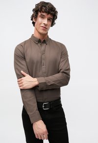 Braunes langärmeliges Hemd aus glattem Stoff mit Standardkragen, Brusttaschenknöpfen und taillierten Ärmeln, kombiniert mit schwarzen Hosen.