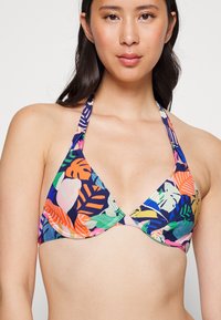 Top de biquíni multicolorido com um padrão de folhas tropicais, formato triangular, amarrações ao pescoço estilo halter e uma textura de tecido suave em tons vibrantes.