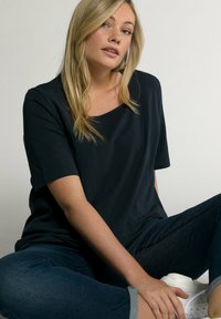Camisetta blu navy a maniche corte con scollo rotondo, texture liscia e vestibilità comoda. Abbinata a jeans scuri con orlo arrotolato e sneakers bianche.