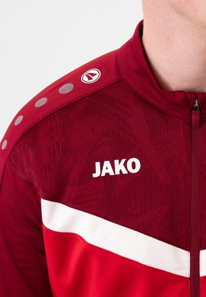 Rote Sportjacke mit weißen Akzenten, strukturiertem Stoff, Reißverschluss und Logo. Besitzt ein gemustertes Design und kreisförmige Schulterdetails.