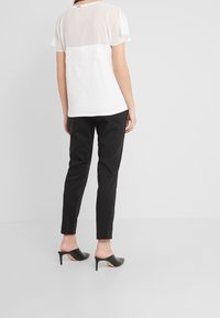 Top bianco a maniche corte con dettagli in pizzo sul retro, abbinato a pantaloni neri aderenti e mule neri con tacco. Tessuto dalla texture liscia.