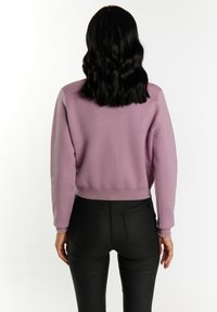 Fialový svetr s croptop designem a dlouhými rukávy, spojený s černými přiléhavými kalhotami s zadními kapsami a hladkým povrchem.