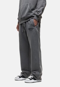 Gray sweatpants with a relaxed fit, featuring side pockets, drawstring waist, and black text logo detail on the left thigh.