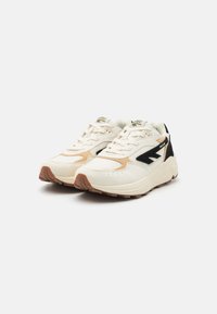 White sneakers with tan and black suede accents, mesh panels, and a textured rubber sole. Features classic lace-up design and logo on tongue.