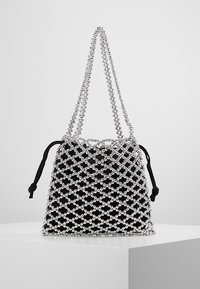 Pochette en tissu noir à l'intérieur d'un sac en filet à perles argentées avec deux poignées en perles et des cordons de serrage noirs de chaque côté.