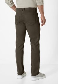 Dark green slim-fit jeans with back pockets, subtle stitching details, and a waistband. Paired with light gray sneakers.