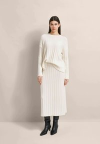 Cremfarbener gerippter Strickpullover und passende Midiyou mit lockerer Passform und langen Ärmeln. Kombiniert mit schwarzen High-Heels.