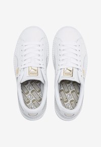 Bílé tenisky s hladkým koženým svrškem, plochými tkaničkami, polstrovaným límcem a zlatými akcenty loga. Texturovaná stélka má geometrický vzor.
