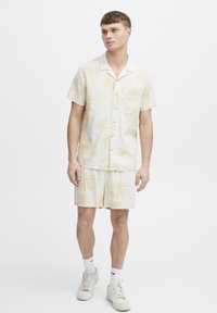 Lightweight beige linen shirt and shorts set with palm tree pattern, featuring a button-down collar and a chest pocket. Sneakers and socks included.
