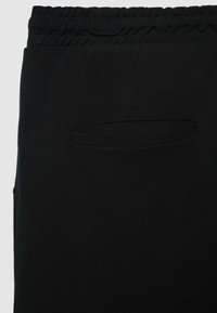 Schwarze Stoffhose mit strukturiertem Gewebe, elastischem Bund und einer kleinen, abgesteppten Gesäßtasche mit horizontaler Öffnung.