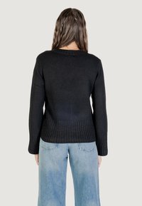Maglione nero lavorato a maglia con orlo e polsini a costine, dotato di scollatura rotonda. Abbinato a jeans a gamba larga blu chiaro. Texture liscia.