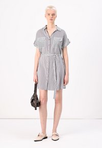 Robe chemise rayée noir et blanc, à manches courtes, fermeture à boutons sur le devant, deux poches poitrine, ceinture à nouer, longueur genou, texture de tissu lisse.