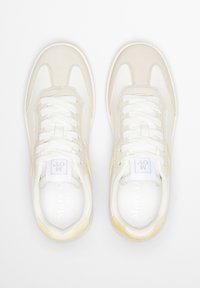 Sneakers beige chiaro con dettagli in mesh bianco e camoscio. Presentano punta tonda, lacci tradizionali e etichetta con il marchio sulla linguetta. Texture liscia.