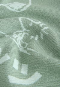 Tissu en maille vert doux avec des visages de chat blancs et des empreintes de pattes dans un motif répétitif, présenté en gros plan avec des plis.