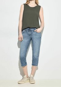 Sleeveless olive green top; light blue, knee-length denim jeans; beige sneakers; casual fit with subtle texture and faded wash.