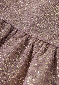 Tejido lila brillante con un patrón texturizado, adornado con lentejuelas doradas. Los detalles de volantes recogidos realzan el diseño.