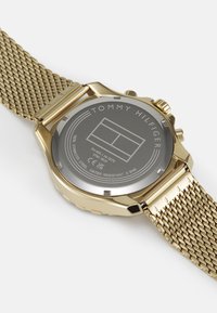 Montre en acier inoxydable doré avec un bracelet en maille. Caractéristiques : un dos argenté avec gravure, étanche jusqu'à 5 bars et un design chronographe.