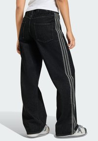 Μαύρο τζιν με φαρδιά μπατζάκια που διαθέτει δύο γκρι κάθετες ρίγες κατά μήκος των εξωτερικών ραφών, με κλασικό σχέδιο πέντε τσεπών και υφασμάτινη υφή.