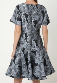 Květin dresses s přiléhavým vrchem a rozšířenou sukní. Černá látka s velkými šedými květinovými vzory. Krátké rukávy a zip na zadní straně.