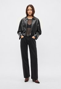 Čierna kožená bunda s golierom, doplnená priesvitným čiernym topom a čiernymi riflemi s vysokým pásom. Celý vzhľad dopĺňajú hnedé čižmy na podpätku.