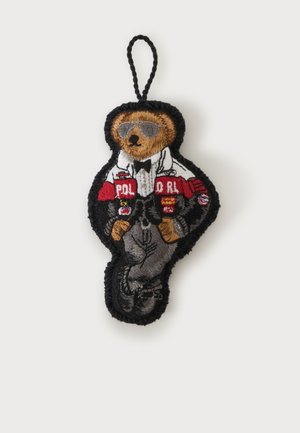 Porte-clés brodé d'un ours portant des lunettes de soleil, une veste blanche avec un texte rouge "Polo RL" et un pantalon gris, avec une boucle noire pour l'accrocher.