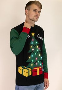 Schwarzer Weihnachtspullover mit einem grünen Baum, der mit bunten Lichtern und einem gelben Stern geschmückt ist, sowie Geschenken in Rot und Gelb am unteren Ende. Rote und grüne Ärmel.