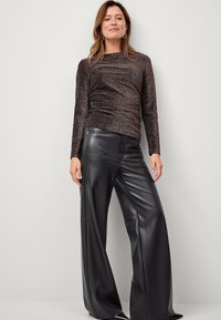 Top lungo a maniche di colore marrone lucido con tessuto testurizzato e design arricciato, abbinato a pantaloni in pelle nera a gamba larga con cuciture eleganti.
