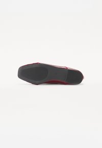 Ballerine rouge avec une tige lisse et brillante et une semelle en caoutchouc noir texturée, présentant un bout pointu et de fines lanières.