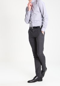 Camicia button-up grigia chiara, pantaloni grigi scuri su misura e scarpe in pelle nere. Tessuto liscio con una forma aderente e texture delicate.