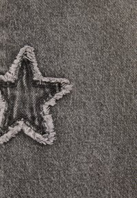 Écusson étoile noire effilochée cousu sur un tissu denim gris texturé, montrant des coutures détaillées et des bords usés.